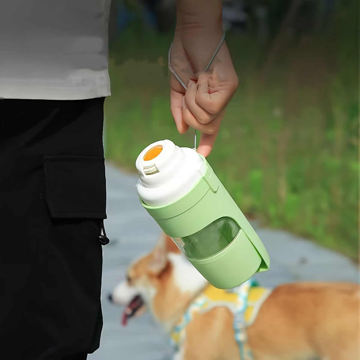 Person carrying a green JMA portable dog water bottle by its strap while walking a dog