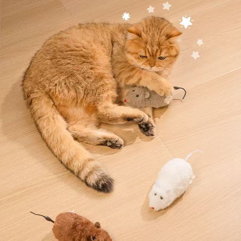 Cat resting with a grey JMA Pet Goods wind-up mouse cat toy, with white and brown mice on the floor